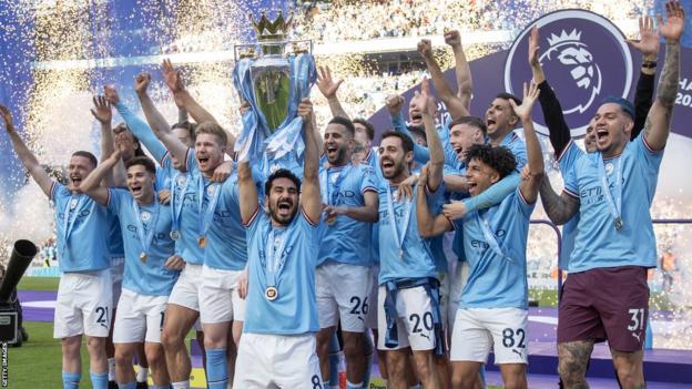 Ilkay Gundogan holds aloft the Premier League trophy as Manchester City team-mates celebrate behind him