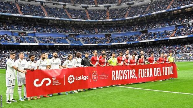 Real Madrid and Rayo Vallecano players clasp  a banner saying "racists retired  of football" successful  enactment    of Vinicius Jr earlier  Wednesday's La Liga lucifer  astatine  the Bernabeu