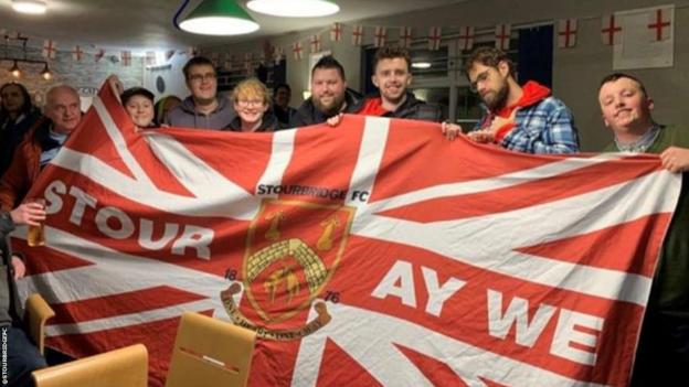 Darts player Michael Smith poses with locals behind a giant Stourbridge FC flag
