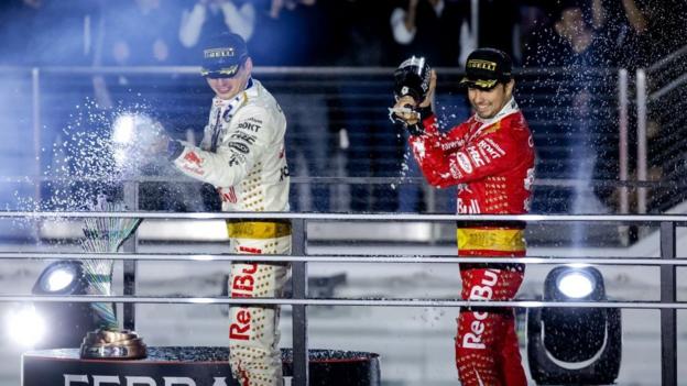 Max Verstappen and Sergio Perez in their Elvis themed race suits on the podium as they spray champagne to their team