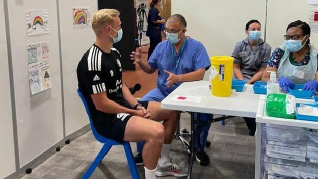 Prof Jonathan Van-Tam prepares to vaccinate Boston United striker Jordan Burrow