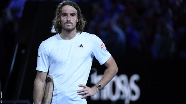 Stephanos Tsitsipas standing with his hands on his hips, his trophy placed under his right arm