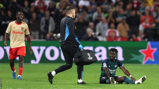 Bukayo Saka waits for treatment in Arsenal's game against Lens