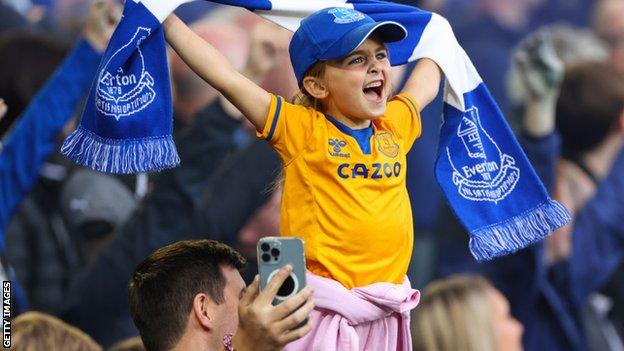 A young girl holds an Everton scarf aloft