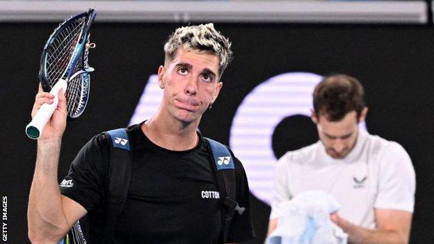 Thanasi Kokkinakis holds up his broken racquet, while Andy Murray looks exhausted at the end of their epic match