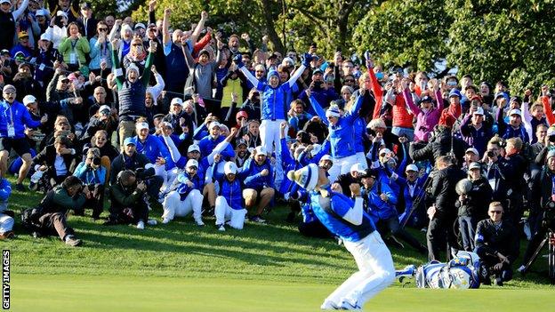 The Europe team rise to their feet along with supporters on the side of the 18th green after Pettersen sinks the winning putt
