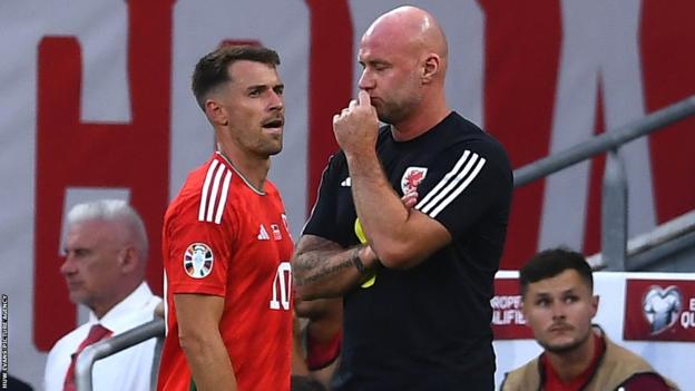 Aaron Ramsey walks behind manager Rob Page after being replaced against Armenia