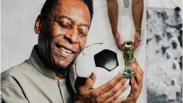A Brazil fans holds a replica World Cup in front of a picture of Pele at at the 2022 World Cup in Qatar