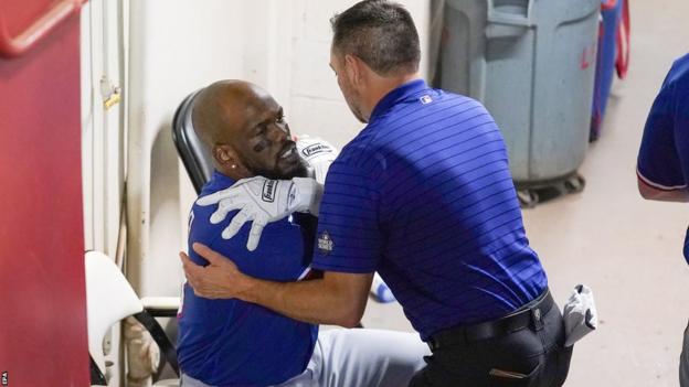 Texas Rangers outfielder Adolis Garcia is treated by a trainer after straining his side batting