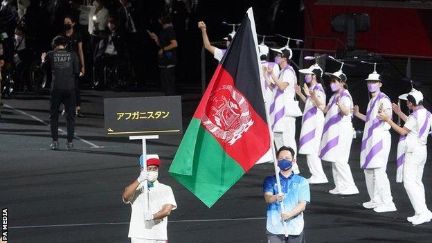 A volunteer carries the Afghan flag at the Tokyo Paralympics opening ceremony