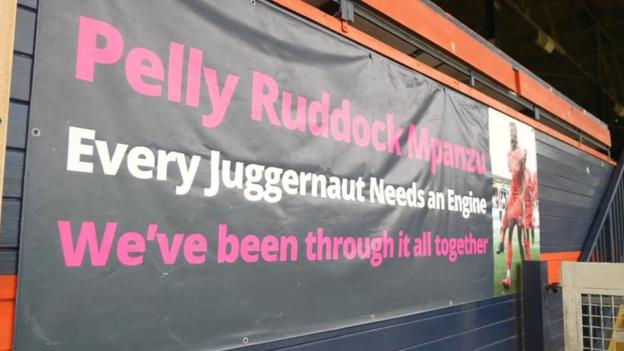 A banner at Kenilworth Road, which reads: "Pelly-Ruddock Mpanzu. Every juggernaut needs an engine. We've been through it all together."