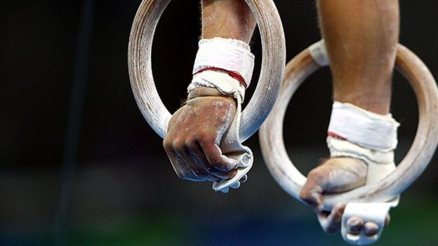 A gymnast holds themselves upright using rings