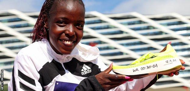 Agnes Tirop poses with a running shoe emblazoned with her 10km world record