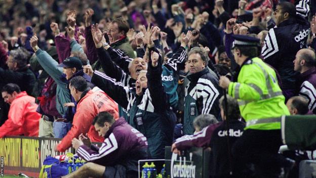 Le banc de Liverpool et les fans célèbrent alors que le manager de Newcastle Kevin Keegan s'effondre dans la pirogue après la défaite 4-3 de son équipe à Anfield en 1996