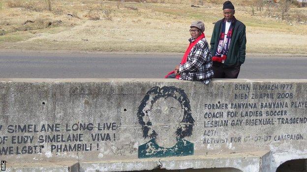 Eudy Simelane's mother, Mali (left) and father Khotso (right) sit on the bridge that was built in honor of their murdered daughter next to a mural of her face on the wall