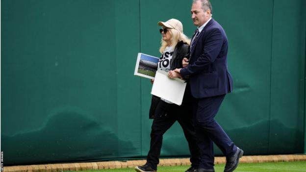 A Just Stop Oil protester is escorted off the court with the empty Wimbledon jigsaw box