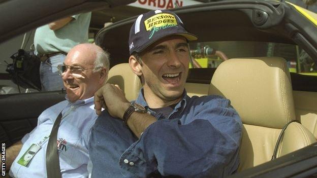 1998: Jordan-coureur Damon Hill uit Groot-Brittannië krijgt een lift van Murray Walker, op de oefendag voor de Grand Prix van Australië in Albert Park in Melbourne, Australië.
