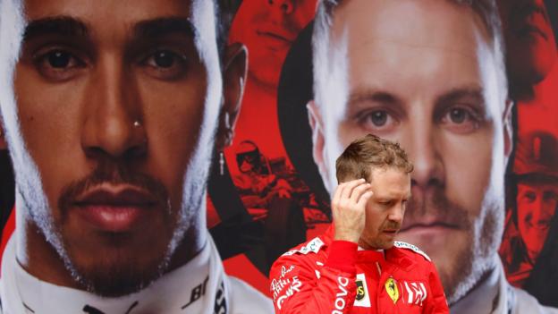 Sebastian Vettel walkes past a giant poster of Lewis Hamilton and Valtteri Bottas