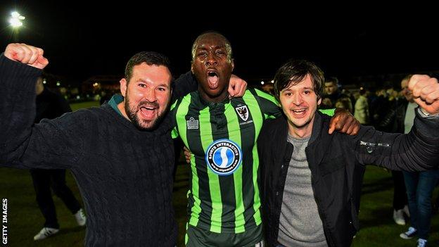 Adebayo Azeez celebrates Wimbledon's play-off victory with two of the club's supporters