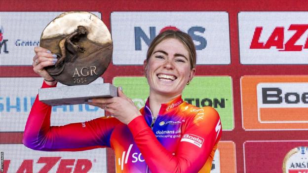 Cyclist Demi Vollering smiles as she holds up the trophy for winning Amstel Gold Race
