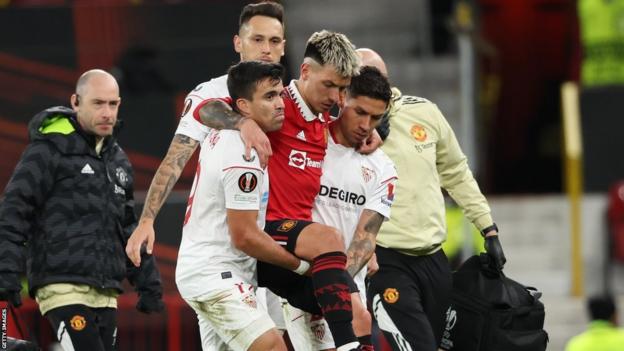 Marcos Acuna of Sevilla and Gonzalo Montiel of Sevilla carry off Lisandro Martinez of Manchester United after an injury during the UEFA Europa League quarterfinal first leg match between Manchester United and Sevilla FC at Old Trafford