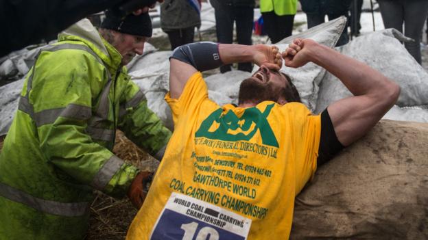A competitor collapses at the finish line of a race at the annual World Coal Carrying Championships in the village of Gawthorpe, near Wakefield, northern England on April 2, 2018