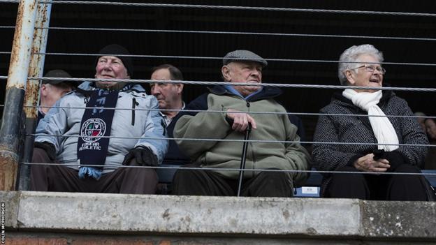 A group of elderly fans in the main stand await the arrival of the teams on to the pitch prior to the kick-off