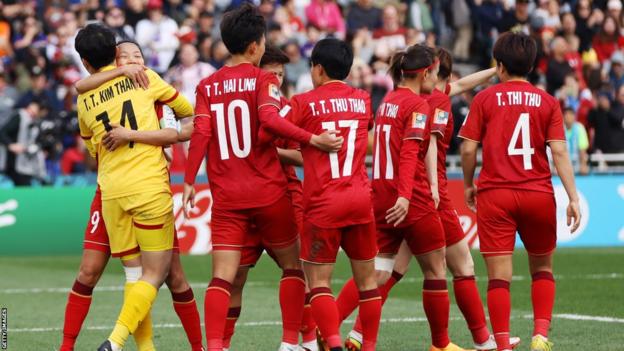 Vietnam keeper Kim Thanh is mobbed by her jubilant team-mates after saving Alex Morgan's penalty