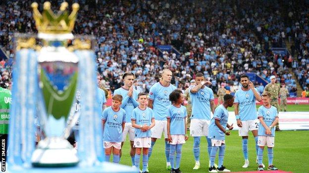 Manchester City players line up behind the Premier League trophy