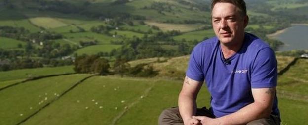 Jake McManus in his climbing gear on top of a mountain looking out to scenery