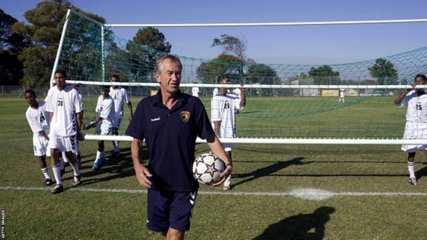 Roald Poulsen walks with ball under arm as boys in kit carry a goal behind him