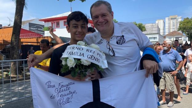 Santos fans Wilson Genio and his son Miguel pose proudly with their Santos flag signed by Pele