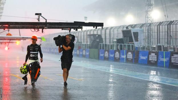 McLaren's Lando Norris walks back to the McLaren pit followed by a cameraman as heavy rain falls at Interlagos