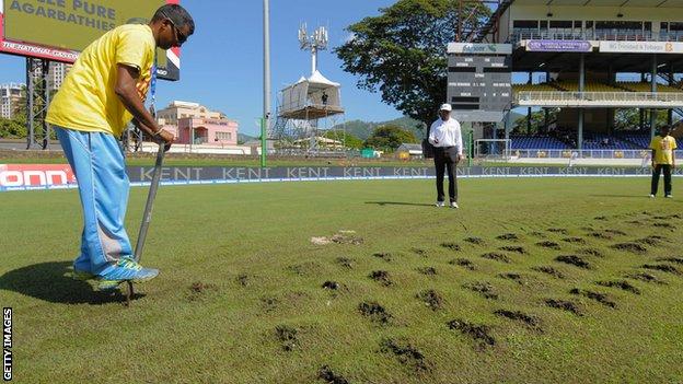 A member of the groundstaff attempts to repair the damaged pitch at Port of Spain