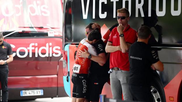 A rider and team members console each other stood next to the Bahrain Victorious team bus