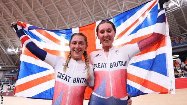 Laura Kenny and Katie Archibald of Team Great Britain celebrate winning a gold medal while holding the flag of they country during the Women's Madison final of the track cycling on day fourteen of the Tokyo 2020 Olympic Games