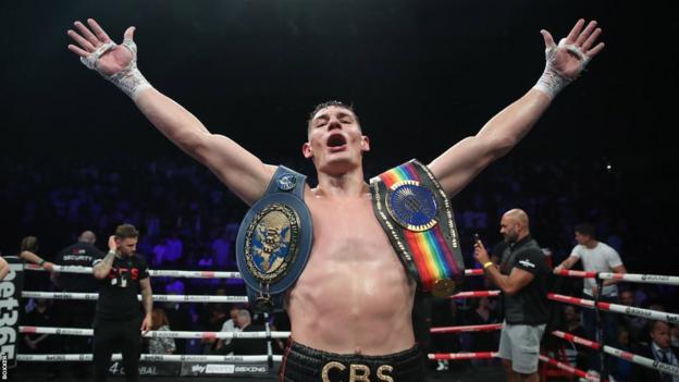 Chris Billam-Smith celebrates with his belts with his arms stretched over his head