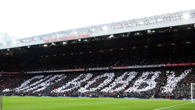 Fans hold up cards to create a mural in remembrance of Sir Bobby Charlton