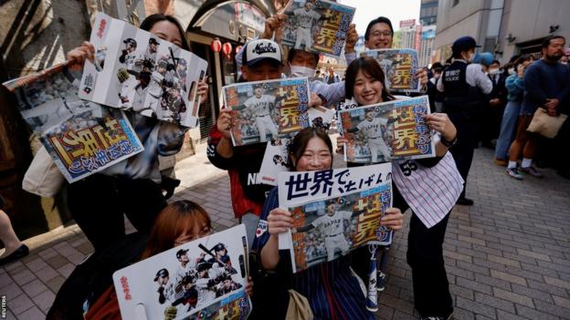 Aficionados sosteniendo periódicos de edición especial que informan sobre la victoria del Clásico Mundial de Béisbol de Japón