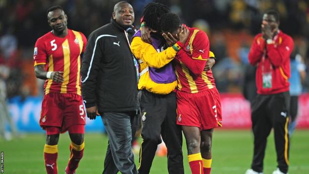 Asamoah Gyan covers his face and cries as team-mates try to console him