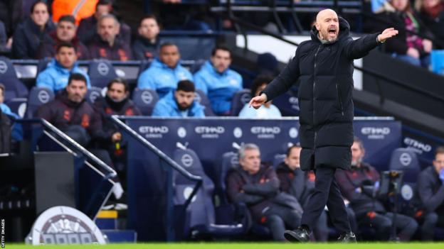 Erik ten Hag stands on the touchline at the Etihad and raises his arm