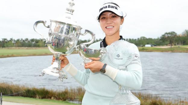 Lydia Ko posing with the Vare Trophy, the Rolex Player of the Year trophy and the CME Globe trophy