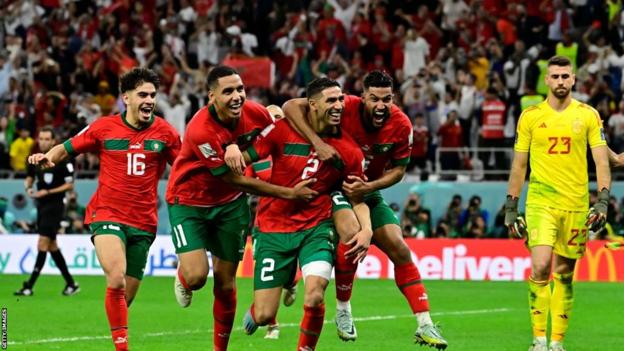 Achraf Hakimi celebrates with his Morocco team-mates while a dejected Unai Simon looks on