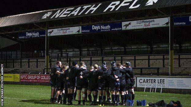 Neath players in huddle below a painted sign on the grandstand at the Gnoll ground
