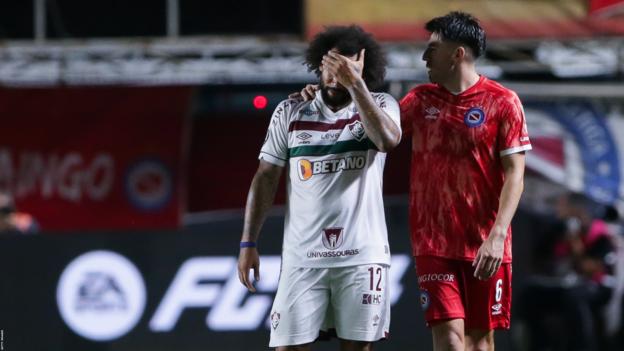 Marcelo of Fluminense is consoled by an Argentinos Juniors player after the injury to Luciano Sanchez