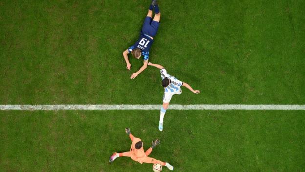 An aerial shot of Julian Alvarez poking the ball past Croatia goalkeeper Dominik Livakovic as defender Borna Sosa lies on the pitch behind the scorer