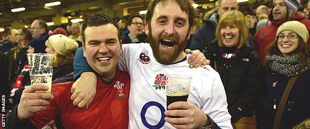 A Wales and an England fan link arm in arm as they share a drink at this year's Six Nations match in Cardiff