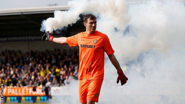 Burton goalkeeper Stephen Bywater clears a smoke bomb from the pitch at the Pirelli Stadium