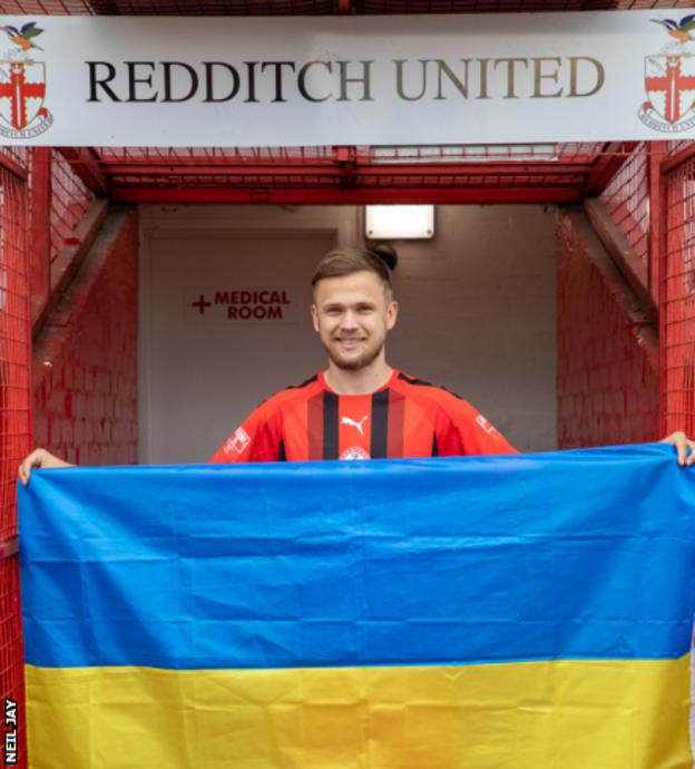 Defender Yan Osadchyi holds the Ukraine flag at Redditch United