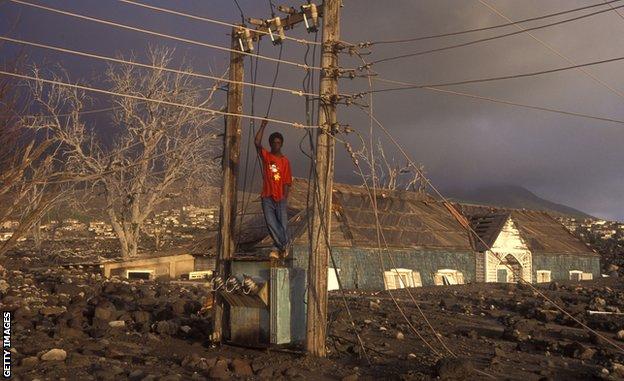 Ten years after the July 1995 eruption, a boy poses on collapsed power infrastructure